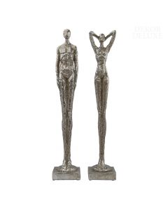 Dekor Deluxe set dveh ločenih podolgovatih srebrnih skulptur moškega in ženske z izrazito dolgimi nogami na podstavku v obliki kvadra.