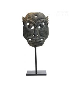 Okultna in zastrašujoča kamnita maska z luknjami in z groznim pogledom na črnem kovinskem, ovalnem podstavku. 