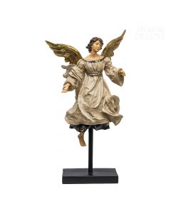 Skulptura ženskega angela z rjavimi lasmi, odprtimi zlatimi krili in plapotajočo bež haljo v letečem položaju na črnem masivnem podstavku.