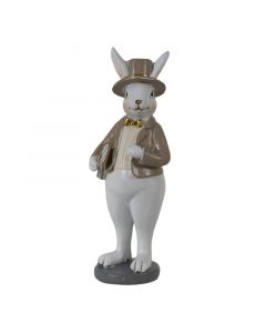 Figura belega velikonočnega zajčka s klobukom in plaščem v rjavi barvi, rumenim telovnikom in s knjigo v roki. 